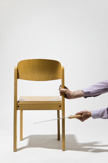 Älterer Mann schneidet Stuhl mit Säge - MUF001358