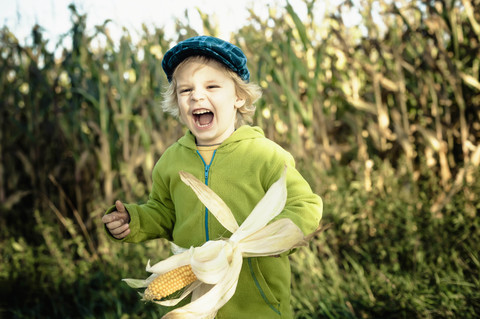 Deutschland, Sachsen, Junge hält Maiskolben und lacht, lizenzfreies Stockfoto