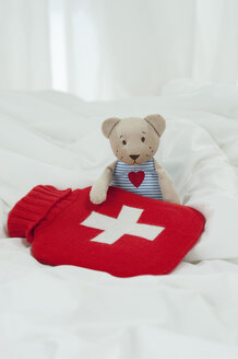 Germany, Bavaria, Teddy bear with hot water bottle on bed - CRF002458