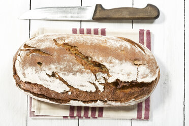 gebackenes Brot mit Serviette und Messer auf Holztisch, Nahaufnahme - MAEF007158