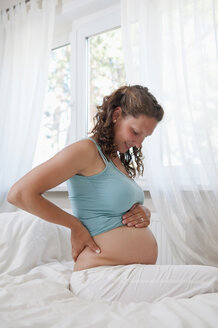 Deutschland, Brandenburg, junge schwangere Frau auf dem Bett sitzend - BFRF000267