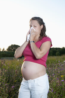 Deutschland, Brandenburg, junge schwangere Frau mit Heuschnupfen steht auf einer Blumenwiese - BFRF000277