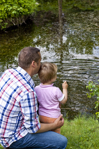 Deutschland, Kiel, Mädchen steht mit seinem Vater an einem Teich und füttert Enten, lizenzfreies Stockfoto