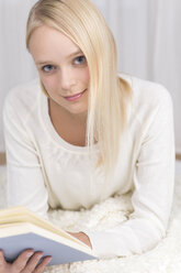 Porträt einer jungen Frau, die auf der Couch liegt und ein Buch liest, lächelnd - DRF000124