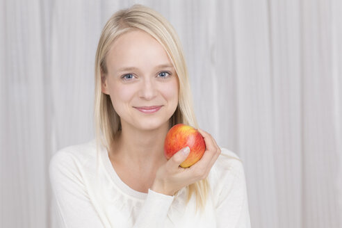 Porträt einer jungen Frau mit einem roten Apfel in der Hand, lächelnd - DRF000129