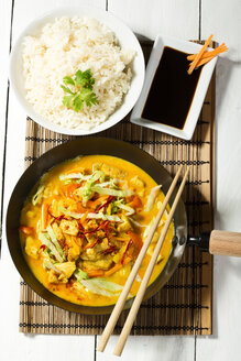 Spicy chicken with red curry, peppers, chillies, carrots, coconut milk and bowl of rice on table mat - MAEF007183