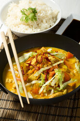 Würziges Hühnerfleisch mit rotem Curry, Paprika, Chilis, Karotten, Kokosmilch und einer Schale Reis auf dem Tischset - MAEF007184