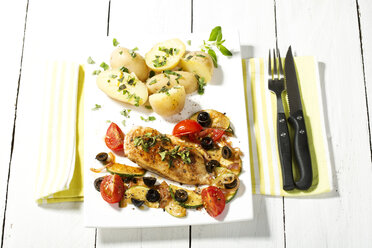 Plate of roasted chicken with potatoes, olives, tomatoes and garnished with herbs on wooden table, close up - MAEF007185