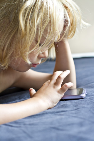Deutschland, Kiel, Mädchen spielt mit Smartphone auf Bett, Nahaufnahme, lizenzfreies Stockfoto