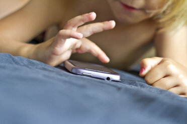 Deutschland, Kiel, Mädchen spielt mit Smartphone auf Bett, Nahaufnahme - JFEF000182