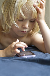 Deutschland, Kiel, Mädchen spielt mit Smartphone auf Bett, Nahaufnahme - JFEF000181