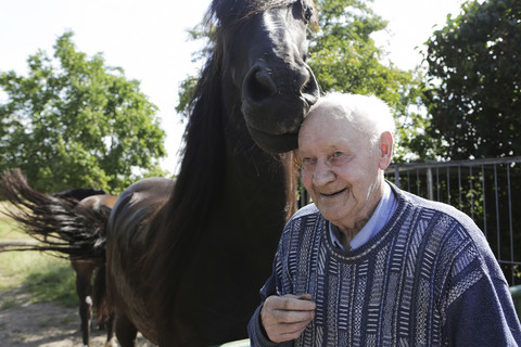 Deutschland, älterer Mann neben Pferd stehend, lächelnd, lizenzfreies Stockfoto