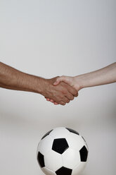 Man and woman shaking hands over soccer ball, close up - KRPF000024