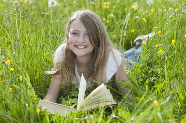 Germany, Bavaria, Portrait of girl lying on meadow and reading book, smiling - CRF002467