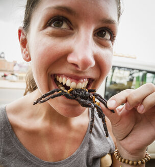 Cambodia, Young woman eating fried tarantula spiders - MBEF000709