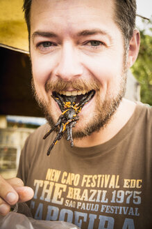 Cambodia, Mid adult man eating fried tarantula spiders - MBEF000710