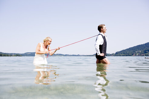 Deutschland, Bayern, Tegernsee, Hochzeitspaar steht im See, Braut hält Bräutigam an der Leine - RFF000089