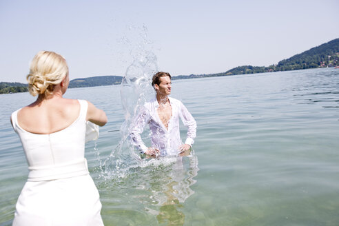 Deutschland, Bayern, Tegernsee, Hochzeitspaar steht im See, gießt Wasser über Bräutigam - RFF000090