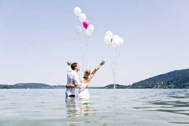 Deutschland, Bayern, Tegernsee, Hochzeitspaar im See stehend, mit Luftballons - RFF000093