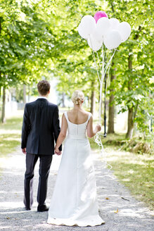 Deutschland, Bayern, Tegernsee, Hochzeitspaar unter Bäumen spazierend, Luftballons haltend - RFF000102