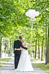 Deutschland, Bayern, Tegernsee, Hochzeitspaar unter Bäumen spazierend, Luftballons haltend - RFF000103