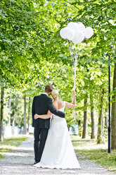 Germany, Bavaria, Tegernsee, Wedding couple walking under trees, holding balloons - RFF000103