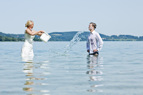 Deutschland, Bayern, Tegernsee, Hochzeitspaar steht im See, gießt Wasser über Bräutigam - RFF000100