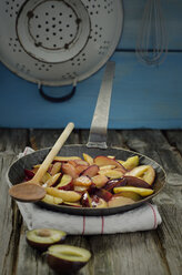 Caramelized prunes in frying pan with wooden spoon and napkin on wooden table, close up - OD000336