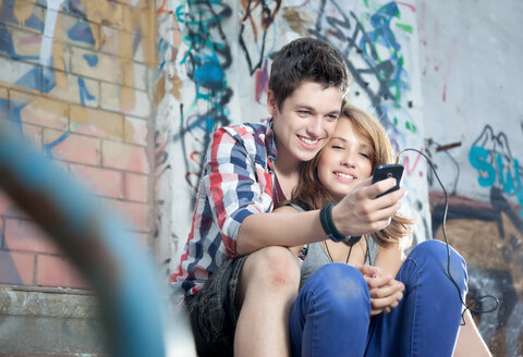 Germany, Berlin, Teenage couple using mobile phone, smiling - MVC000008