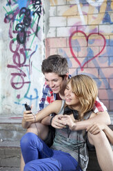 Deutschland, Berlin, Jugendliches Paar mit Handy, lächelnd - MVC000012