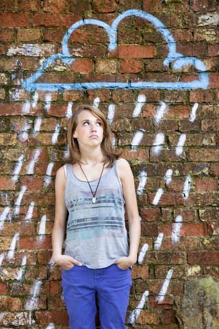Deutschland, Berlin, Teenager-Mädchen steht vor Backsteinmauer mit Graffiti, lizenzfreies Stockfoto