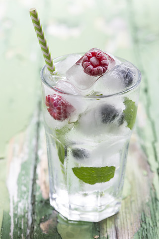 Glas mit Beeren in Eiswürfeln mit Minzblättern auf Holztisch, Nahaufnahme, lizenzfreies Stockfoto