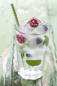 Glas mit Beeren in Eiswürfeln mit Minzblättern auf Holztisch, Nahaufnahme - STB000011