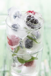 Glas mit Beeren in Eiswürfeln mit Minzblättern auf Holztisch, Nahaufnahme - STB000012