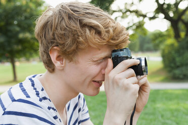 Junger Mann, der mit einer altmodischen Kamera ein Foto im Park macht - TCF003571