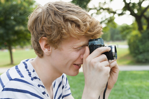 Young man taking a picture in park with an old-fashioned camera - TCF003571