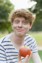 Young man eating an apple outdoors - TCF003569