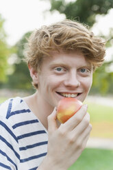 Junger Mann isst einen Apfel im Freien - TCF003568