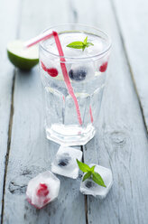 Glas Mineralwasser mit Eiswürfeln und gefrorenen Beeren auf Holztisch, Nahaufnahme - ODF000364