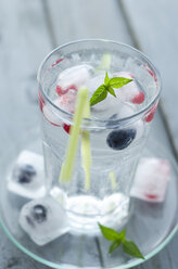 Glas Mineralwasser mit Eiswürfeln und gefrorenen Beeren auf Holztisch, Nahaufnahme - ODF000365