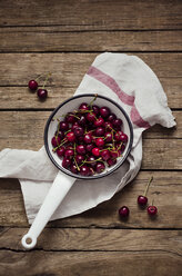 Fresh sour cherries in a colander on a wooden table - CZF000073