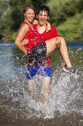 Germany, Baden-Wuerttemberg, Winterbach, athletic young man carring young woman while running through Rems river - STSF000124