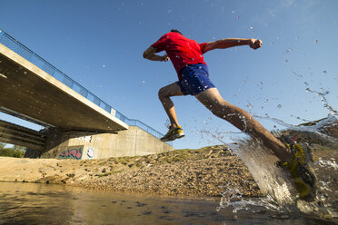 Germany, Baden-Wuerttemberg, Winterbach, athletic young man running through Rems river - STSF000118