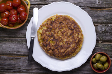 Potato tortilla with tomatoes and olives on wood table, close-up - ODF000413