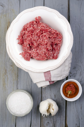 Rohes Rinderhackfleisch, Meersalz, Knoblauch und Paprika auf dem Holztisch, lizenzfreies Stockfoto
