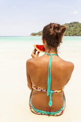 Thailand, Koh Surin island, woman eating a slice of watermelon at the white sandy beach - MBEF000734