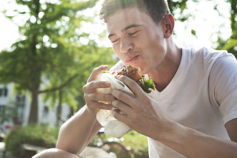 Junger Mann beim Essen eines Hamburgers, lizenzfreies Stockfoto