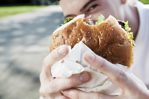 Junger Mann zeigt seinen Hamburger, lizenzfreies Stockfoto