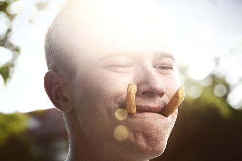 Junger Mann mit zwei Pommes frites im Mund - FEXF000040