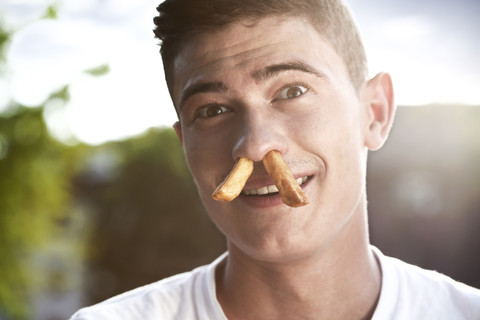 Junger Mann mit zwei Pommes frites in der Nase, lizenzfreies Stockfoto